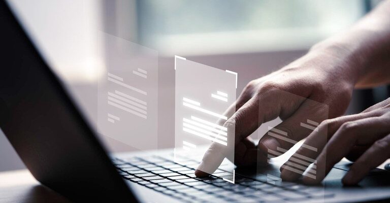 Mãos digitando em um laptop com ícones de documentos flutuando, sugerindo uma interface digital. Ao fundo, uma janela desfocada com luz natural.