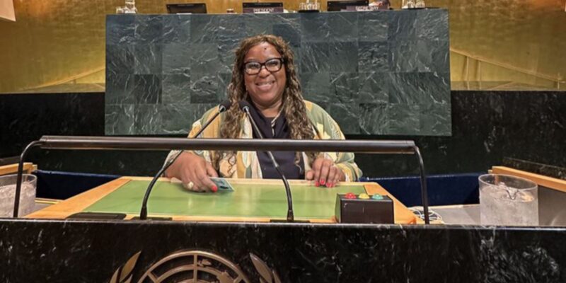 Ministra Macaé, mulher negra, sorrindo na bancada principal da Assembleia Geral da ONU.