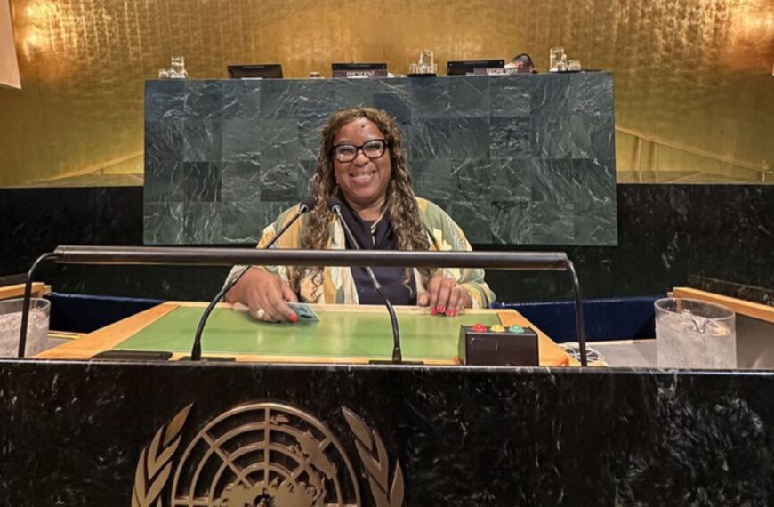 Ministra Macaé, mulher negra, sorrindo na bancada principal da Assembleia Geral da ONU.