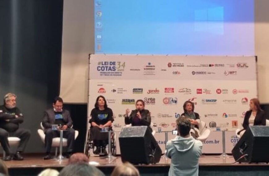 Mesa de debate sobre Lei de Cotas com seis pessoas no palco e plateia assistindo.