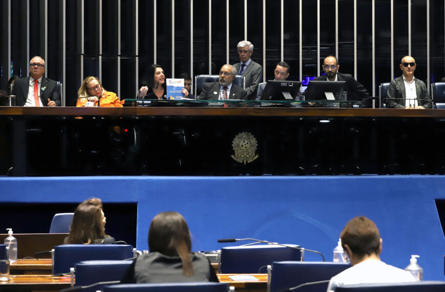 Sessão no Senado com autoridades na mesa diretora e pessoas assistindo ao fundo.