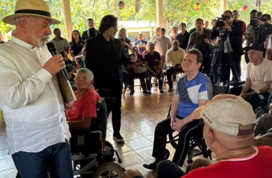 Presidente Lula discursa para cadeirantes em evento social, rodeado por público e imprensa.