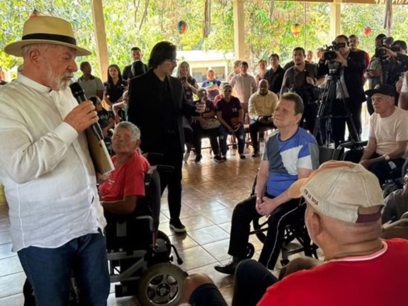 Presidente Lula discursa para cadeirantes em evento social, rodeado por público e imprensa.