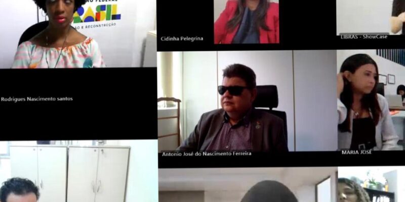 Videoconferência formal com 8 participantes, diversidade de gênero e intérprete de LIBRAS presente.