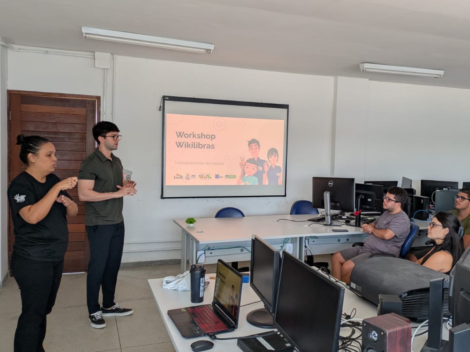 Workshop sobre Wikilibras com intérprete de Libras e participantes em sala de informática.