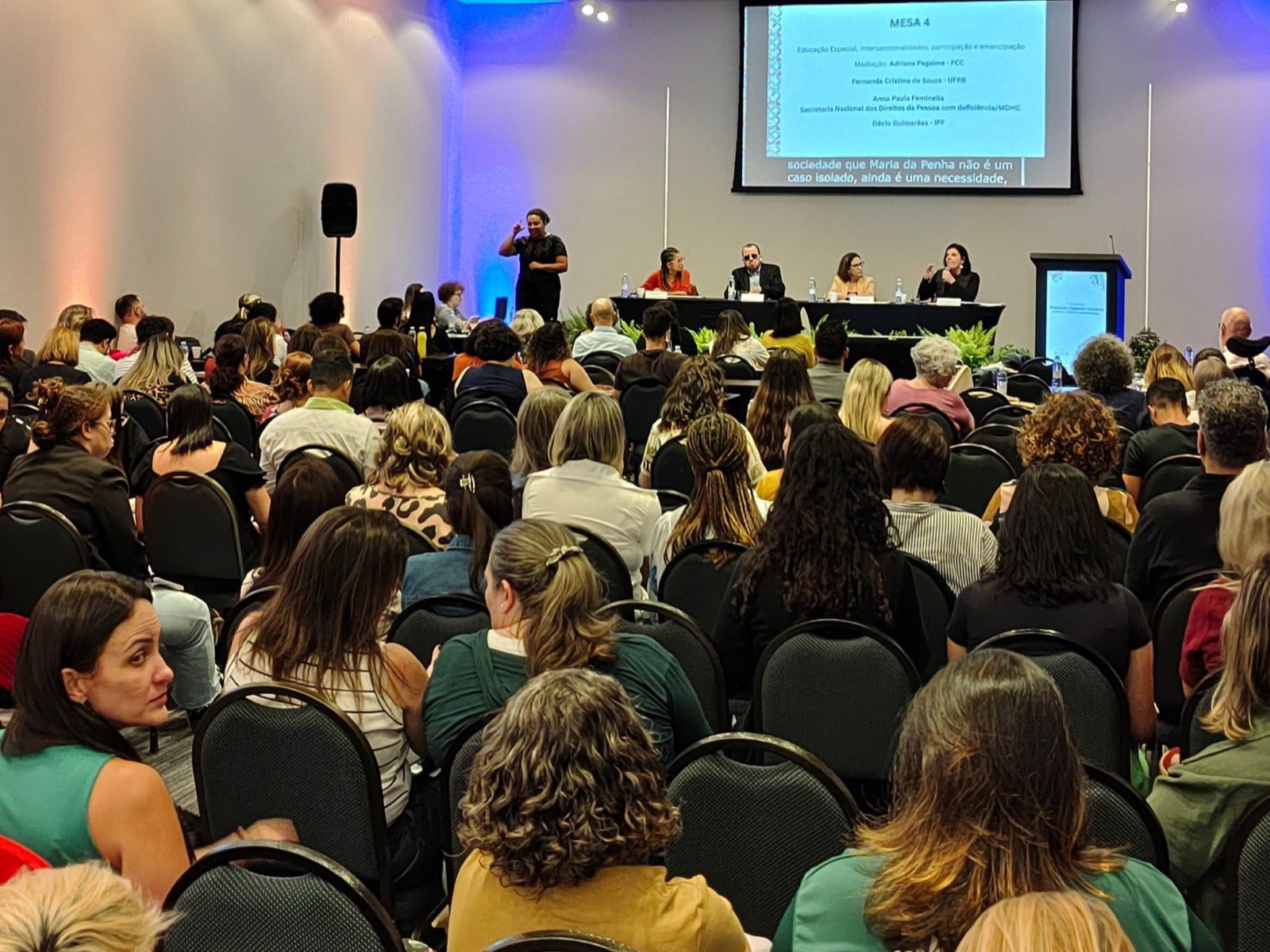 Auditório cheio com pessoas assistindo a um painel de debates sobre educação especial.