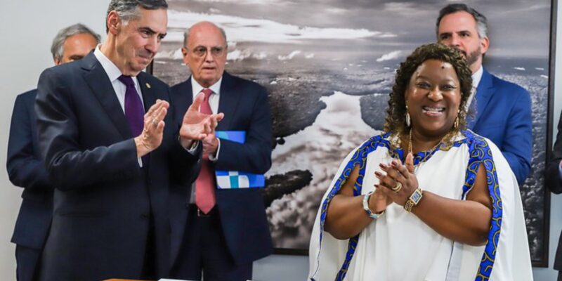 Ministra Macaé e ministro Barroso sorrindo, aplaudindo juntos em evento solene, em pé.