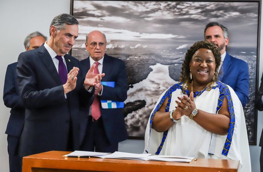Ministra Macaé e ministro Barroso sorrindo, aplaudindo juntos em evento solene, em pé.