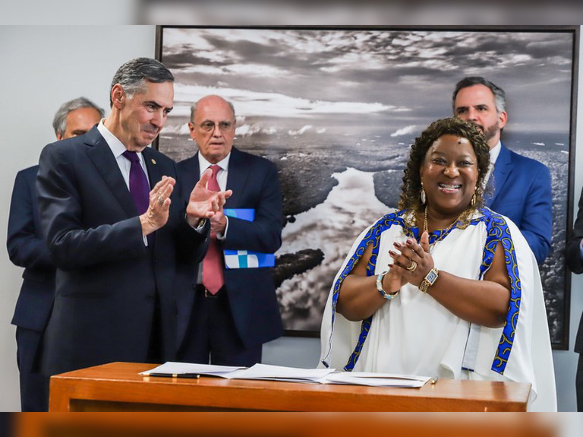 Ministra Macaé e ministro Barroso sorrindo, aplaudindo juntos em evento solene, em pé.