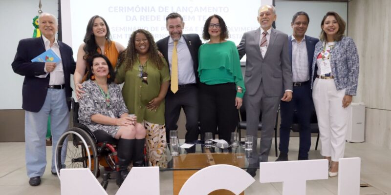Grupo de nove pessoas posa sorrindo em evento oficial sobre autismo, à frente das letras MCTI.