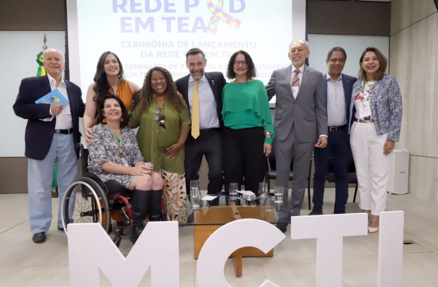 Grupo de nove pessoas posa sorrindo em evento oficial sobre autismo, à frente das letras MCTI.