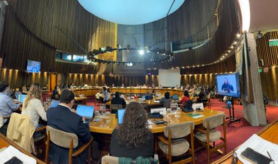 No Chile, Brasil reforça compromisso com políticas baseadas em evidências para ampliar direitos das pessoas com deficiência Sala de reunião ampla, pessoas sentadas ao redor de mesas, com notebooks e tela com intérprete de Libras.