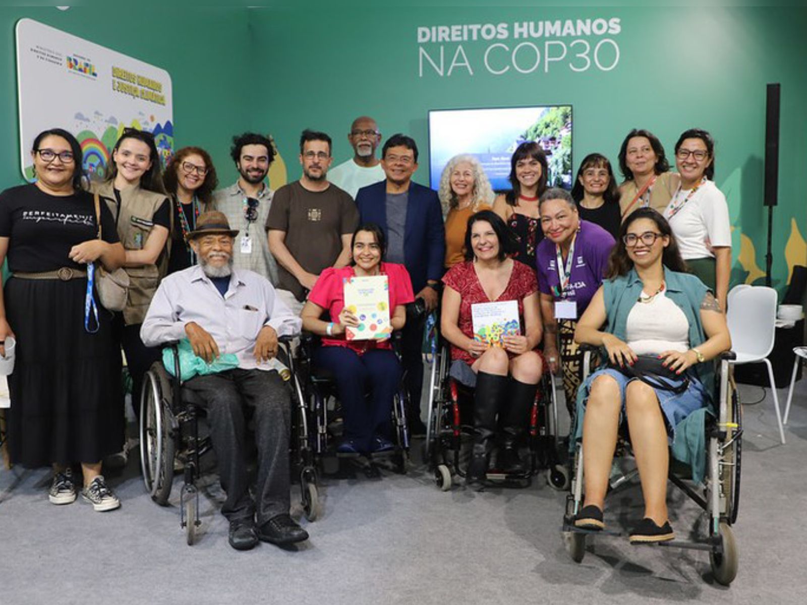 Grupo diverso, com pessoas em cadeiras de rodas, sorrindo em evento sobre direitos humanos na COP30.