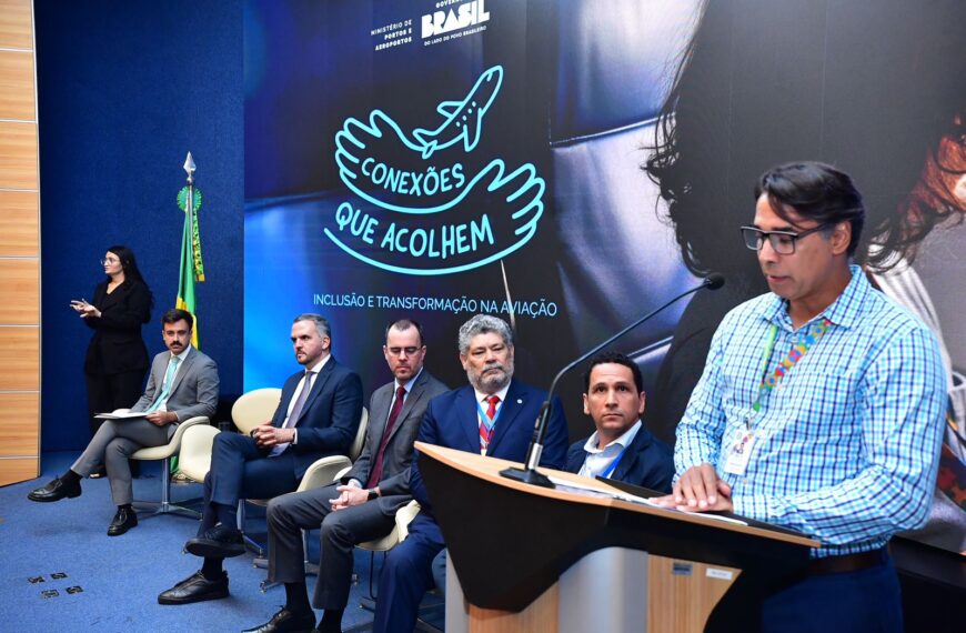 Evento formal com painel “Conexões que acolhem”, homens de terno sentados e um homem discursando.