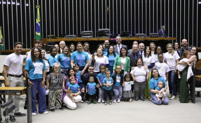 Grupo diverso com adultos e crianças posando sorridentes no plenário da Câmara dos Deputados.