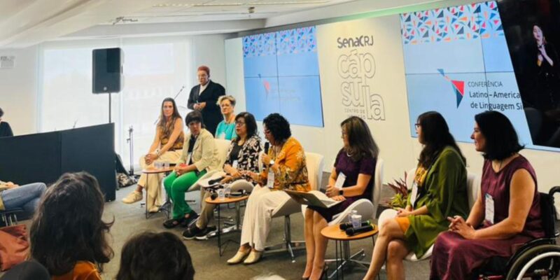 Mesa de debate com seis pessoas, incluindo uma mulher em cadeira de rodas, no evento do Senac RJ.