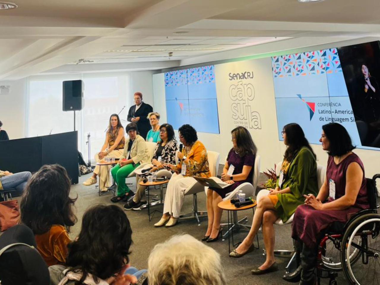 Mesa de debate com seis pessoas, incluindo uma mulher em cadeira de rodas, no evento do Senac RJ.