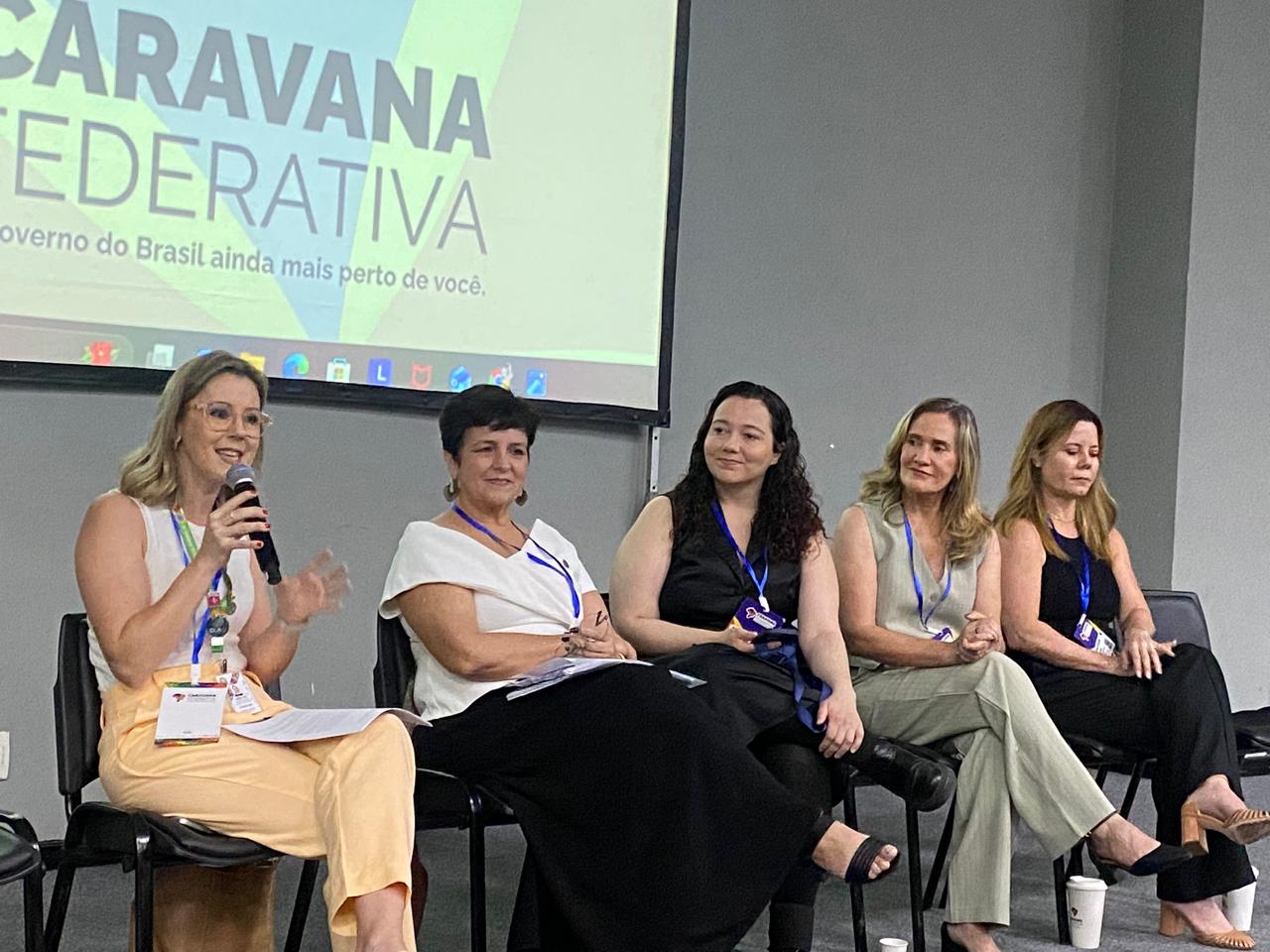 MDHC defende ampliar participação das mulheres nos espaços de poder, ao integrar Caravana Federativa Cinco mulheres sentadas participam de um painel em um evento chamado "Caravana Federativa". Uma delas fala ao microfone, todas usam crachá e vestem roupas sociais. O ambiente é formal e fechado.