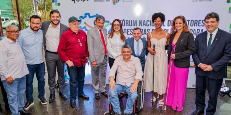 Grupo diverso posa sorrindo em evento de inclusão do Governo do Piauí. Destacam-se um homem em cadeira de rodas e duas mulheres com bengalas para deficientes visuais. Clima de celebração.