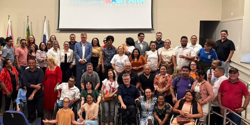 Grupo de homens e mulheres posa para foto em auditório, incluindo pessoas com deficiência, como usuários de cadeira de rodas. Ao fundo, tela com logomarca do Governo do Pará e bandeiras.