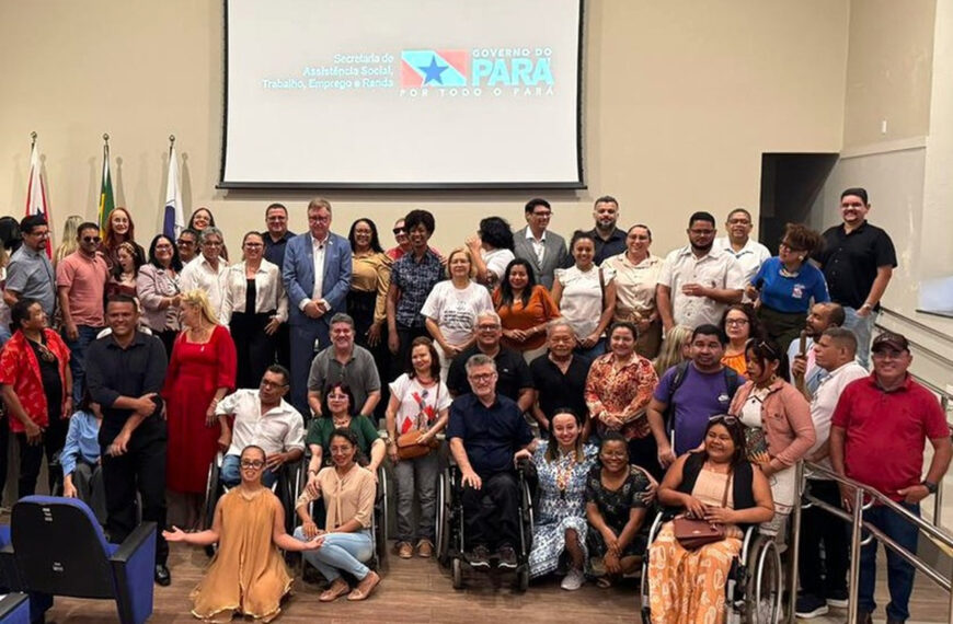 Grupo de homens e mulheres posa para foto em auditório, incluindo pessoas com deficiência, como usuários de cadeira de rodas. Ao fundo, tela com logomarca do Governo do Pará e bandeiras.
