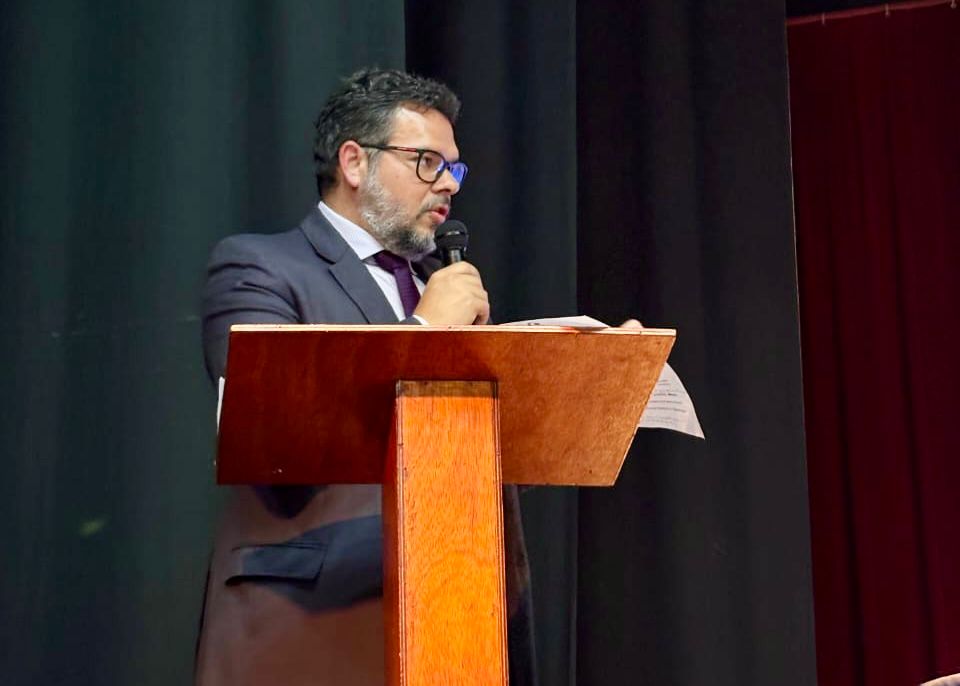 Governo do Brasil e Instituto Benjamin Constant ampliam acesso à tecnologia assistiva e marcam nova etapa do Novo Viver sem Limite Alex Reinecke, diretor de Relações Institucionais da Secretaria Nacional dos Direitos da Pessoa com Deficiência (SNDPD), está em pé, de terno e gravata, falando ao microfone atrás de um púlpito de madeira, segurando folhas. Ao fundo, cortinas escuras e vermelhas indicam ambiente de evento formal.